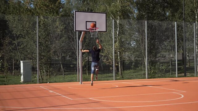 Caucasian man with leg injury dribbles basketball on court, shoots at hoop and misses. Acute pain from injury during amateur player training after unsuccessful jump. Effort and willpower of person.