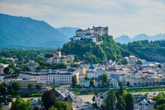 Salzburg Cathedral church and Hohensalzburg Fortress stand above old town rooftops with mountains behind Salzburg, Austria