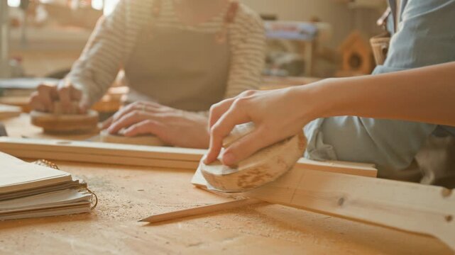 Close-up view of anonymous girl and boy sanding pieces of wood with hand sanders while learning woodworking skills during craft lesson with unrecognisable teacher