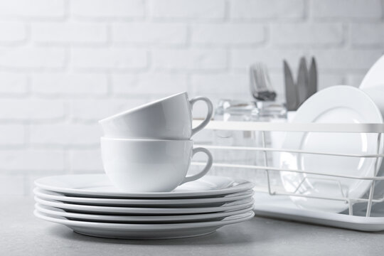 Set of clean dishes, glasses. cutlery and drying rack on light grey table, closeup
