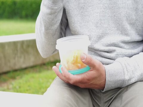 A person opens a clear plastic container filled with sliced fruit, showcasing common food storage methods linked to chemical leaching.