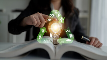 Obraz premium Spark of Innovation: A Business Person Holding a Light Bulb Over an Open Book with Eco-Friendly Icons Representing Sustainability and Energy Solutions Quark.
