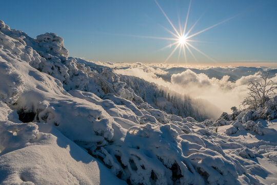 View of Salatin mountain peak covered in deep snow under a bright winter sun with a starburst effect and clouds in the valley Liptovska Stiavnica, Zilinsky kraj, Slovakia.