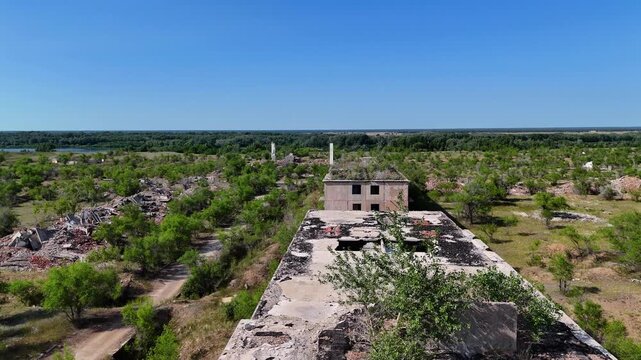Low altitude drone flight over a damaged roof of an abandoned panel house overgrown with bushes. View of surrounding building ruins in Chagan ghost town. Post-apocalyptic landscape of a former secret 