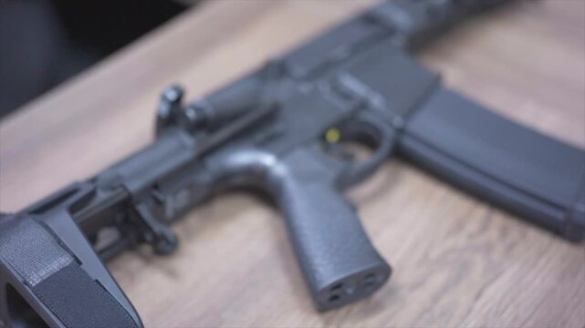 Close-up of Black Assault Rifle with Tactical Sight Resting on Wooden Surface