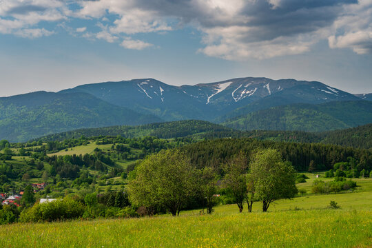 View of the rolling green hills and Low Tatras mountains with snow patches under a cloudy sky near Horna Lehota, Banskobystricky kraj, Slovakia.