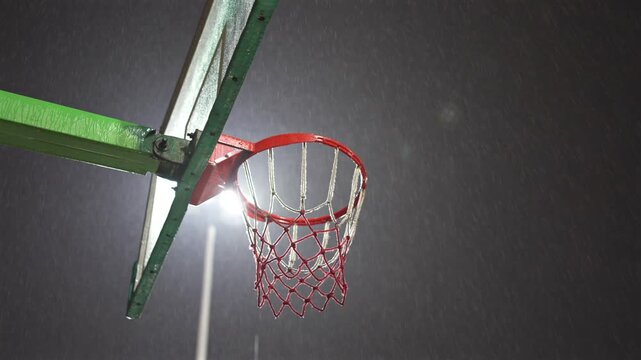 Nighttime Basketball Hoop with Red Rim and Net Illuminated by Bright Light Against Dark Sky