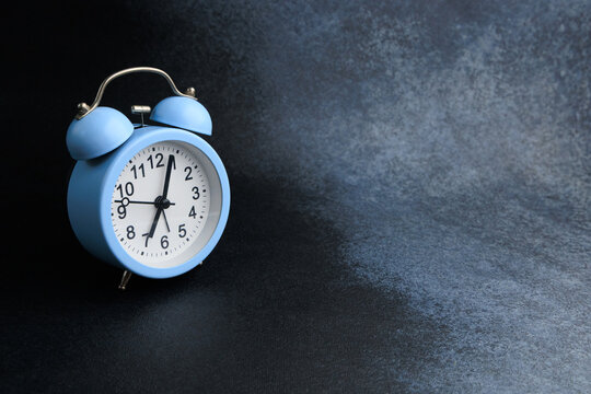 Bright blue alarm clock resting on a dark textured surface while time ticks away in an artistic display of simplicity