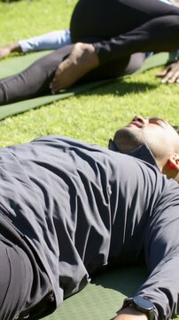 Vertical video: Pausing after cue, man in top breathing supine on green mat on lawn with smartwatch