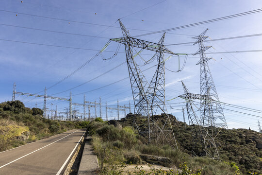 View of the Aldeadavila II Electrical Substation with high-voltage transmission towers and power lines along a rural road under a clear blue sky in Aldeadavila de la Ribera, Castile and Leon, Spain.