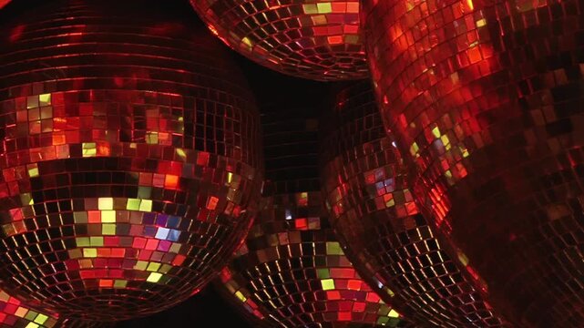Multiple glittering disco balls reflect a vibrant array of red, blue, and gold lights, creating a festive and energetic atmosphere at a Christmas celebration inside a bustling nightclub.