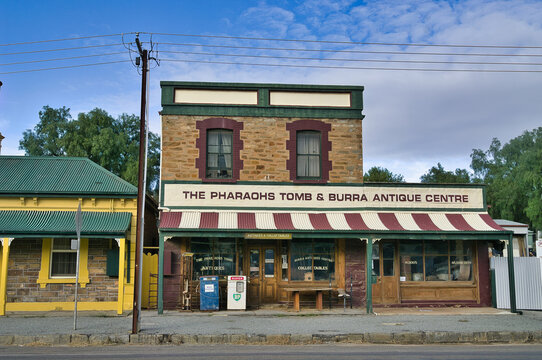 A charming facade of an antique and collectibles store, with a classic striped awning, old windows, and a vintage BP petrol pump. In the town of Burra, South Australia, 