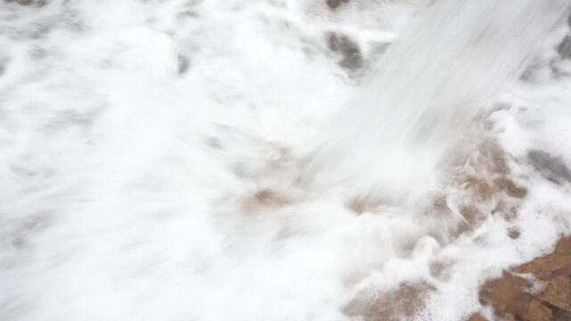 Extreme close-up of a powerful water stream crashing into a muddy dirt basin, creating intense white foam and turbulence. Ideal abstract B-roll for flooding, irrigation, and water extraction.