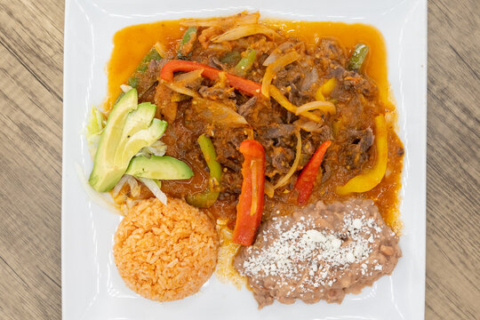 Overhead view of hearty plate of bistec steak smothered in ranchero sauce, beans, and rice to satisfy that urge for a Mexican food meal