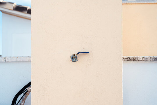 Minimalist photograph of a small outdoor faucet on a white wall. Image focused on side perspective, clean composition and object recognition for artificial intelligence and computer vision.