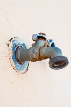 Close-up photograph of a worn outdoor metal faucet with textured white wall. Ideal image for artificial intelligence datasets, object recognition and perspective studies.