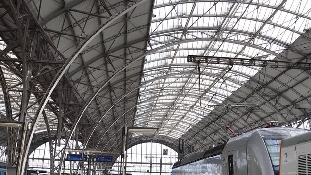 Historic railway station with giant steel arches and modern electric train beneath glass roof showing industrial transport architecture and urban mobility