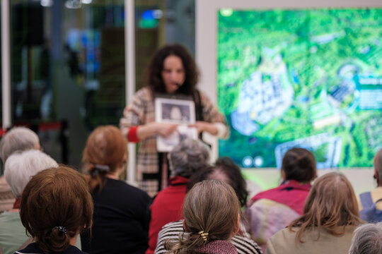 Group of older adults listening during community presentation, presenter points at photo, explains local project.