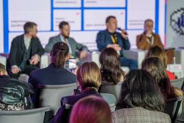 Obraz premium Audience watches panel discussion at business conference, attendee records speakers with smartphone, networking vibe and focused engagement.