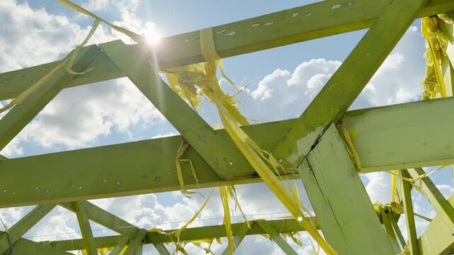 Bright sunbeams filter through a decaying green wooden structure tangled with frayed yellow fabric. The glowing clouds and worn beams evoke a hopeful yet lonely feeling of passing time.