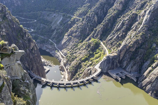 View of the Aldeadavila Dam and its curved wall nestled between steep granite cliffs and winding roads in the Duero River canyon Aldeadavila de la Ribera, Castile and Leon, Spain.