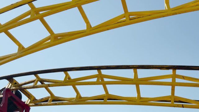 Bright yellow steel roller coaster tracks curve upward toward the sky. The colorful structure brings a sense of anticipation and pure excitement for a thrilling ride on a sunny summer day.