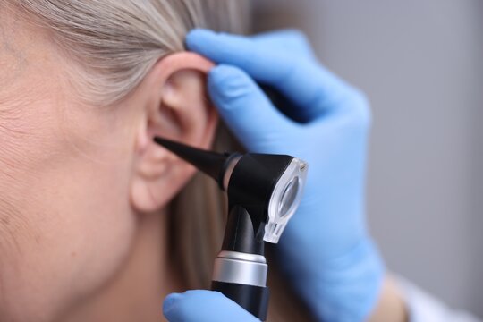 Hearing test. Doctor examining woman's ear with otoscope in clinic, closeup