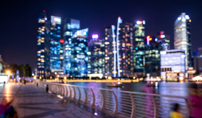 Obraz premium A blurred cityscape view of a skyline at night featuring illuminated buildings reflecting on the water with a walkway in the foreground.