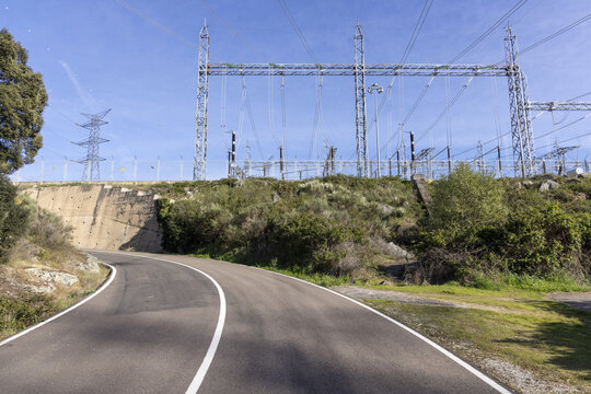View of the Aldeadavila II Electrical Substation with high-voltage power lines and towers above a winding road and green vegetation in Aldeadavila de la Ribera, Castile and Leon, Spain.