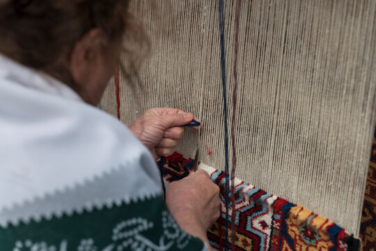 Close-up of a craftsman's hands weaving a traditional Azerbaijani carpet on a vertical loom. Detailed process of manual knotting and rug making.