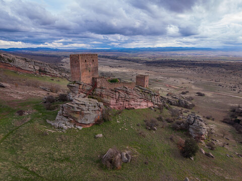 Castle of Zafra, a medieval fortress perched on red sandstone rocks in Guadalajara, Spain, with vast Castilian plateau and dramatic cloudy sky stretching to distant mountains