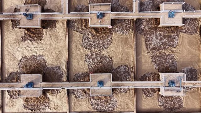 Top-down view of multiple bioreactor aeration basins at a municipal wastewater treatment facility showing activated sludge process with surface aerators mixing brown turbulent effluent