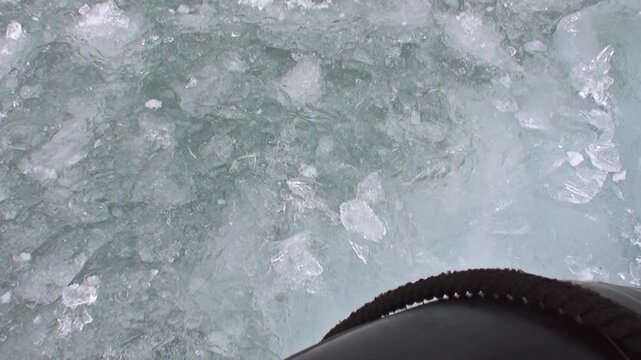 Sturdy boot carves path through shimmering, fragmented ice floes in cold waters of Arctic Ocean, off coast of Norway. Frigid environment creates captivating display of movement.
