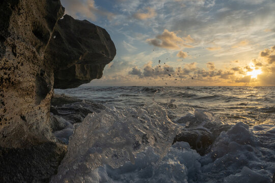 View of ocean waves crashing against dark coastal rocks with sea spray under a golden sunrise sky Florida, United States.