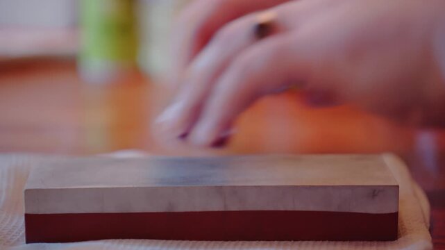 Close up shot of person using a whetstone to sharpen a chef&rsquo;s knife