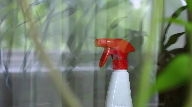 Plastic Spray Bottle for Home Plant Care Behind Glass with Green Leaves