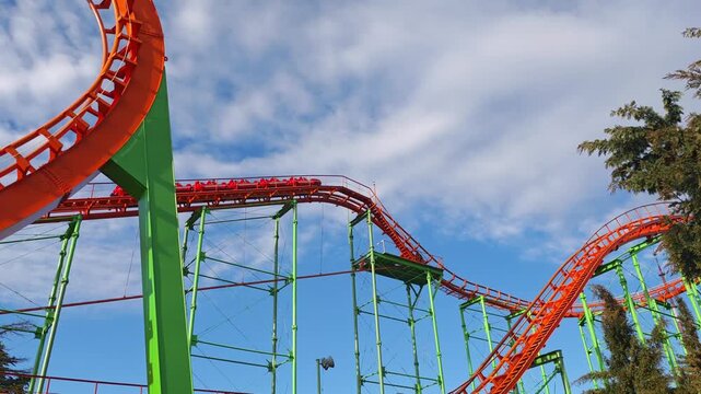 Red roller coaster car going down a thrilling track at an entertainment park. Exciting ride against a beautiful blue sky with clouds