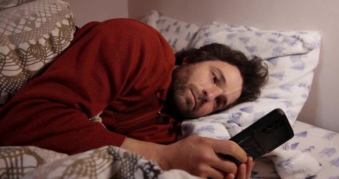 Tired man using a smartphone before sleeping