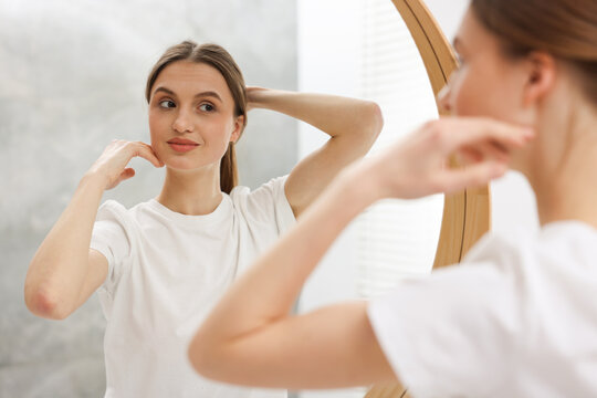Beautiful young woman looking at herself in mirror indoors, selective focus