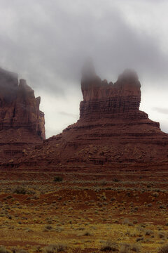View of the iconic red sandstone buttes of Monument Valley partially shrouded in low clouds and mist under an overcast sky Oljato-Monument Valley, Arizona, United States.