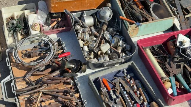 Used tools displayed on asphalt, assorted secondhand hand tools and small parts spread across open toolbox and plastic trays