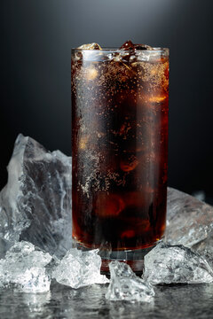 Cola with ice in misted glass on a black stone table.