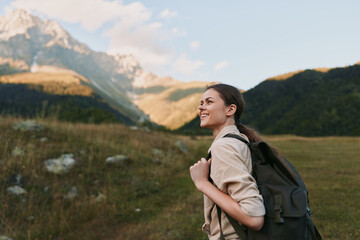 Naklejka premium An outdoor woman with a backpack stands in a mountain valley, smiling into the distance. A lifestyle portrait capturing hiking, travel, and nature curiosity.
