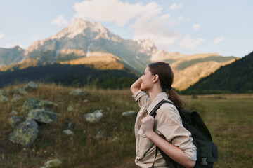 Naklejka premium Woman hiker with backpack admires distant alpine peaks in a wide meadow, enjoying a calm outdoor lifestyle moment and fresh mountain air. She explores rugged scenery.