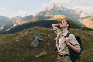 Naklejka premium Cheerful woman hiking outdoors, backpack on, sunlit mountain landscape, relaxed posture, gentle breeze, vivid wildflowers, natural colors, vast scenery, wide sky above