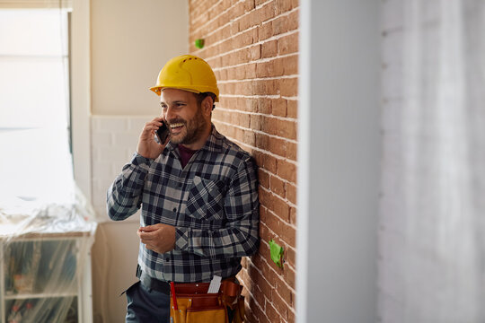 Happy worker talking on cell phone at construction site.