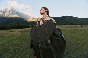 Naklejka premium A young woman hiker with a large backpack stands in a wide meadow, mountains in the background, conveying determination, anticipation, and a spirit of adventure.