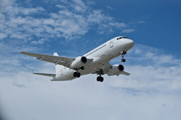 Obraz premium White Airplane Approaching for Landing Against Blue Sky with Clouds