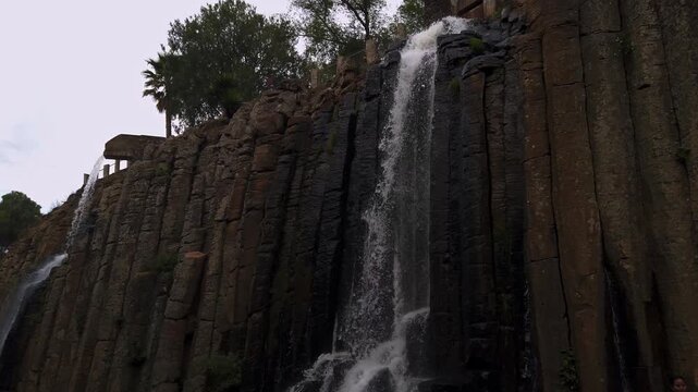 Tilt down shot capturing water cascading over tall basalt rock formations, strong vertical texture and natural flow creating dramatic outdoor landscape scene