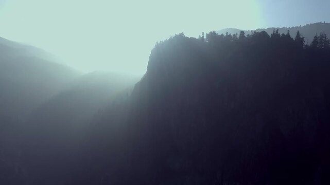 Drone pulls back over misty mountains with sun rays in Valle de Guadalupe